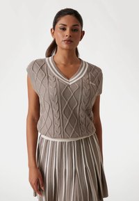 Beige knitted sleeveless top with cable pattern and V-neck, paired with a pleated skirt featuring white stripes along each pleat.