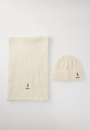 Ribbed cream knit scarf ja matching beanie, joka sisältää pienen kirjailtua logoa kummassakin. Pehmeä rakenne ja joustava istuvuus.