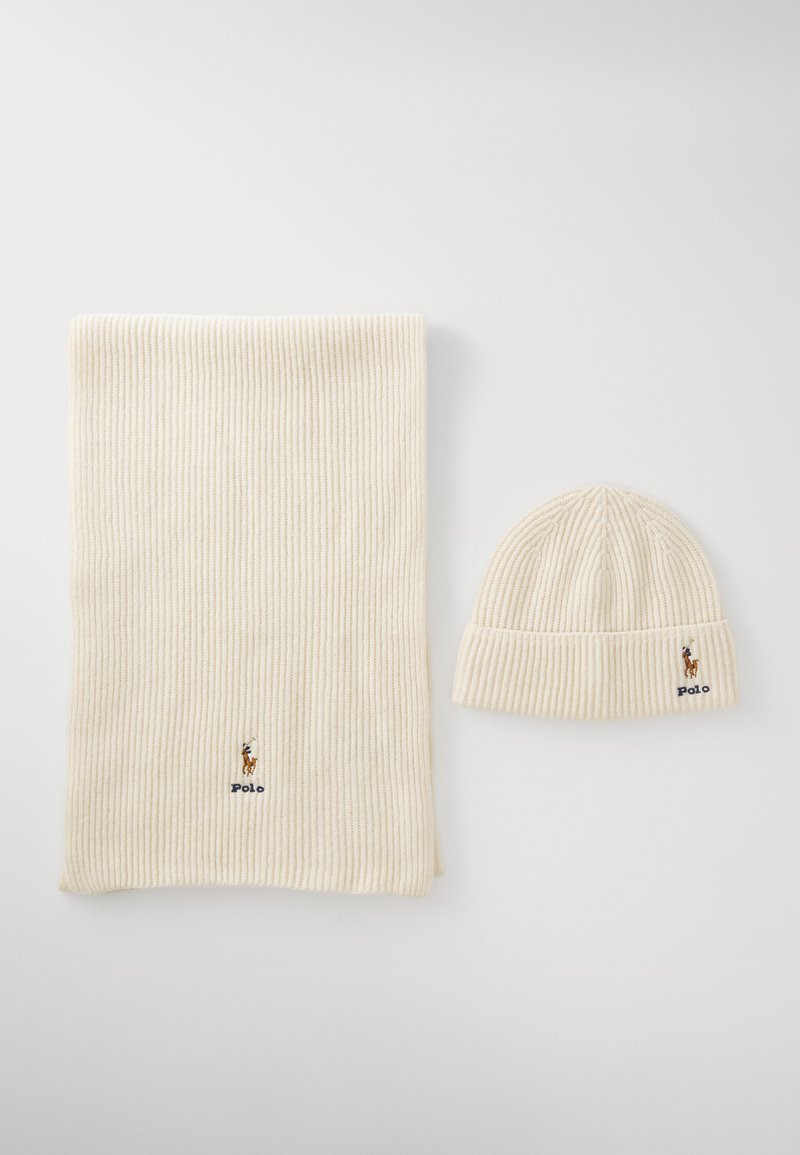 Ribbet krem strikket skjerf og matchende lue, med en liten brodert logo på begge. Myk tekstur med en elastisk passform.