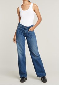 Lätt vit linne topp kombinerad med vida blå jeans. Jeansdärmen har en klassisk tvätt, femficksdesign och subtil blekning. Svarta skor.