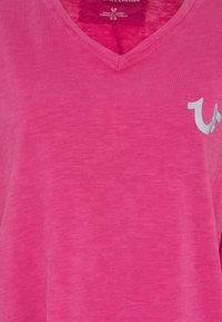 Roze V-hals T-shirt van zachte, lichtgewicht stof met een subtiele heatherpatroon en een klein zilverkleurig logoaccent aan de voorkant.