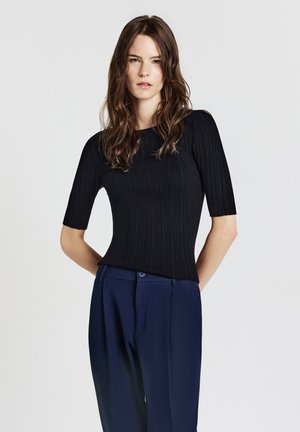 Top nero a coste con maniche corte, caratterizzato da un collo rotondo e abbinato a pantaloni blu navy a vita alta. Texture liscia e design aderente.