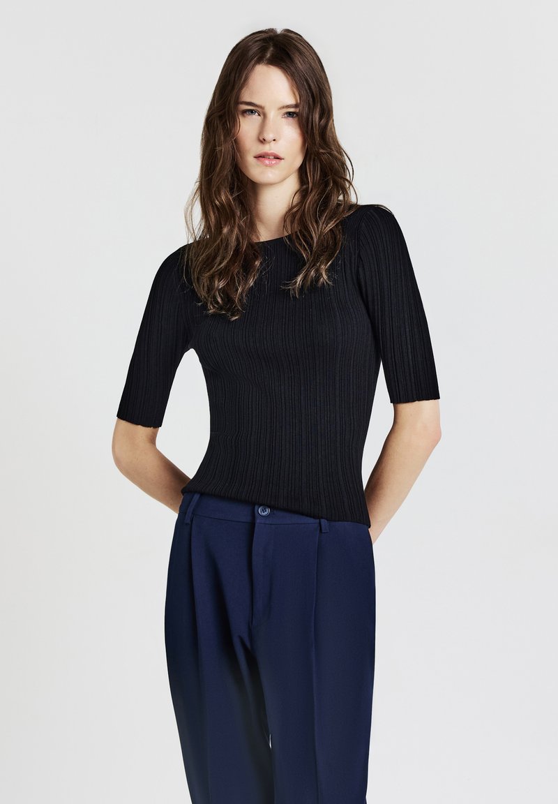 Top nero a coste con maniche corte, caratterizzato da un collo rotondo e abbinato a pantaloni blu navy a vita alta. Texture liscia e design aderente.