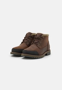 Botas de cuero marrón con un collar acolchado, punta redondeada, acentos de goma negra en la parte delantera y una suela texturizada para tracción.