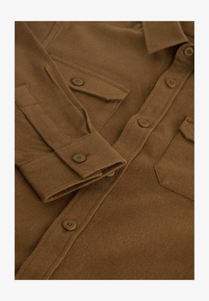 Hnedá košeľa s gombíkmi vyrobená z jemného, textúrovaného materiálu, ktorá má dve náprsné vrecká a gombíkové manžety. Gombíky sú hnedé a okrúhle.