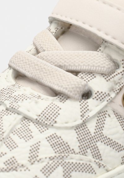 White sneaker featuring a textured design with beige accents, flat laces, and a plastic strap. Notable details include a patterned surface.