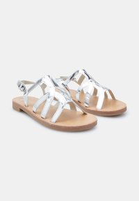 Zilveren metalen sandalen met meerdere kruislings geplaatste banden, open teenontwerp en een platte tan zool. Heeft een verstelbare gesp op de enkelband.