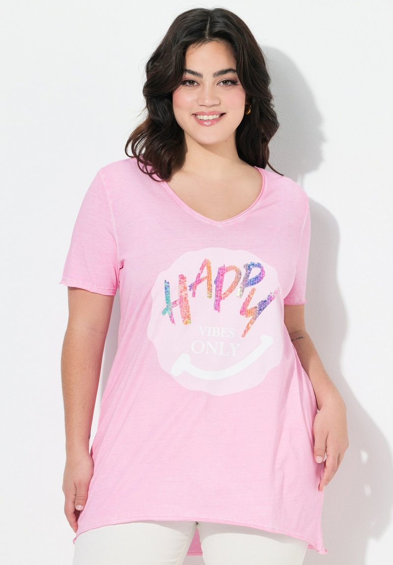 Camiseta rosa de manga corta con escote en V y un gráfico de una cara sonriente. El texto "SOLO BUENAS VIBRAS" está adornado con lentejuelas coloridas. Tejido suave y casual.