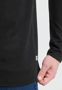 Must have mustriga musta särk pikad varrukad, millel on sile tekstuur ja ümaral serv. Külje peal on väike logo silti, mis sobib hästi juhuslike siniste teksadega.