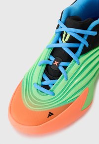 Chaussures de sport avec un design vert et orange, tige texturée, languette en mailles noires, lacets bleus et logo de marque bien en évidence.