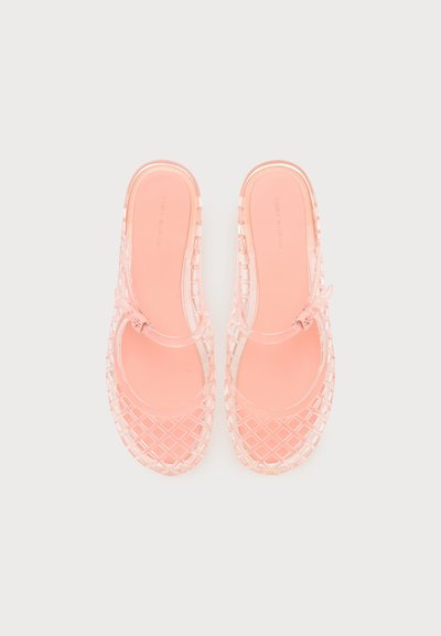 Ζευγάρι ροζ διαφανή ζελέ σανδάλια με σχέδιο σταυρωτού μοτίβου και ρυθμιζόμενους λουρίδες στον αστράγαλο σε απλό ανοιχτόφωτο φόντο.