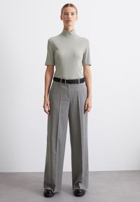 Svetlo siva kratkotrajna turtleneck majica u kombinaciji sa sivim širokim hlačama, naglašena crnim remenom. Glatka tkanina i kroj prilagođen telu.
