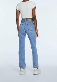 Jeans rectos de color azul claro con cintura alta, acabado de denim desgastado y bolsillos traseros. Combinados con una camiseta blanca corta y zapatillas blancas.