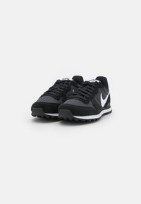 Scarpe da atletica nere con tomaia in suede e rete, caratterizzate da un logo swoosh bianco, chiusura con lacci e suola in gomma testurizzata.