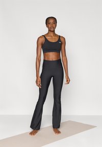 Reggiseno sportivo nero e leggings a vita alta svasati, realizzati in materiale elastico, caratterizzati da una texture liscia e un design minimalista.