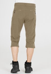 Knälängd, beige byxor med en slät yta, utrustade med bakfickor och dragkedjedetaljer, som bärs med svarta vandringskängor.