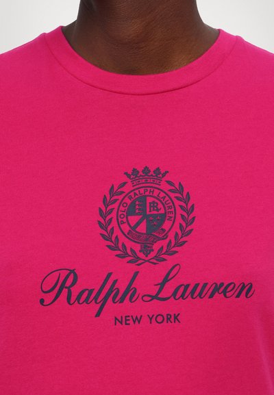 T-shirt de algodão cor-de-rosa com um logótipo azul-marinho com um design de coroa e louro, exibindo "Ralph Lauren" e "NEW YORK" em tipografia elegante.