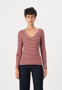 Langärmliges Oberteil mit V-Ausschnitt in burgunderrot und cremefarbenen Streifen. Gerippte Textur mit taillierter Silhouette, kombiniert mit dunkler Jeans.
