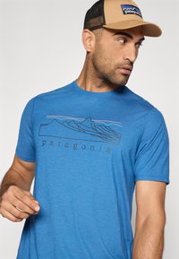 Μπλε κοντομάνικο μπλουζάκι με μαύρη γραμμική ζωγραφιά βουνών και τη λέξη «patagonia» με πεζά γράμματα από κάτω.