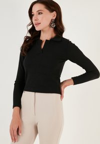 Black ribbed long-sleeve top with a collared neckline, worn with beige pants. Features a fitted design and smooth, textured fabric.