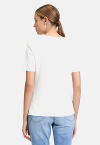 T-shirt blanc à manches courtes avec une coupe décontractée, texture lisse et un design simple. Le dos est uni sans détails ni graphiques supplémentaires.