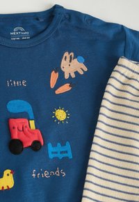 Chemise en coton bleue pour tout-petit, ornée de motifs brodés colorés représentant un lapin, des carottes, un tracteur, un soleil et le texte « petits amis ». Manches rayées.