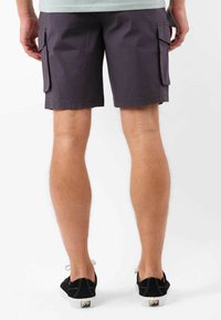 Shorts cargo violets en tissu tissé, avec poches latérales et coupe droite, associés à des baskets noires.