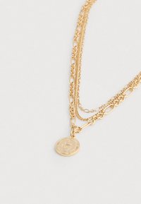 Colar de corrente dourada multicamadas com vários estilos de elos e um pendente redondo com desenho de coroa em relevo.