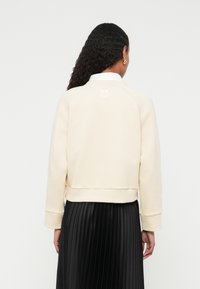 Crèmekleurige sweatshirt met geribbelde manchetten en zoom, voorzien van een subtiele logo-borduring op de achterkant, gecombineerd met een zwarte geplooide rok.