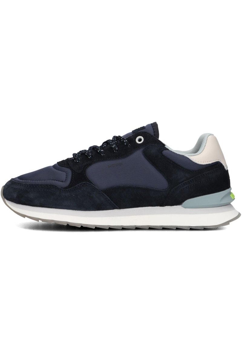 Marineblauwe sneakers met suede en mesh, voorzien van een witte tussenzool, zwarte veters en een onderscheidende groene accent aan de hiel.