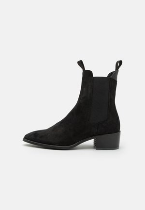 Czarne zamszowe botki za kostkę z elastycznymi panelami bocznymi, w szpic oraz niskim obcasem blokowym. Posiada pętelki ułatwiające zakładanie. Teksturowana powierzchnia.