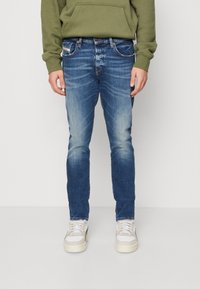 Bleka blå denimjeans i slim fit med femfickorsdesign. Bärs med en grön hoodie och vita sneakers, med detaljerad sömnad.