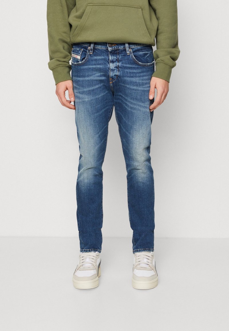 Bleka blå denimjeans i slim fit med femfickorsdesign. Bärs med en grön hoodie och vita sneakers, med detaljerad sömnad.