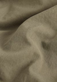 Tessuto verde oliva con una superficie liscia e testurizzata, caratterizzato da delicate coste e morbide pieghe, che riflettono la luce in sottili variazioni.