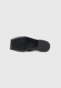 Black leather shoe sole with a smooth finish. Square toe design, flat heel, and embossed logo detail in the center. Minimalist style.