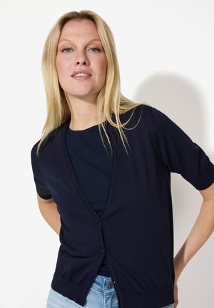 Marineblauer kurzärmliger Cardigan mit tiefem V-Ausschnitt, Knopfschluss und strukturiertem Strick. Kombiniert mit einem passenden dunklen Oberteil und hellblauen Jeans.