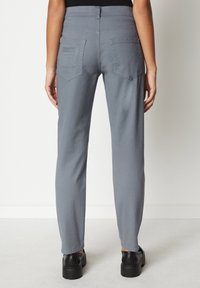 Pantalones gris de longitud tobillo confeccionados en una tela suave, con dos bolsillos traseros y un diseño de pierna recta, combinados con zapatos de plataforma negros.