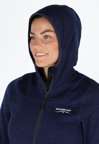 Felpa con zip di colore blu navy, con una superficie morbida, dotata di cappuccio e zip nera. Logo "SWEDEMOUNT" ricamato sul petto.
