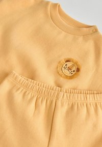 Ljusgul bomullsoutfit med en ribbad halsringning, elastisk midja och ett broderat lejonmotiv på toppen.