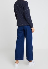 Námořnický blazer s malými bílými vzory kotev, spárovaný s širokými džíny v prostředním modrém odstínu a bílými teniskami.