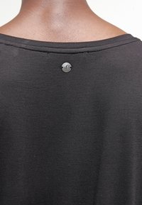 Camiseta de tela negra que muestra una textura suave y lisa con un cuello redondo y un pequeño acento metálico circular en la parte posterior que presenta 's0'.