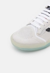 Kengät, joissa on vaaleanharmaa mokkanahka päällinen, valkoiset verkkoyksityiskohdat, rei'itetty varvaskotelo, valkoiset nauhat ja läpikuultava kumipohja.