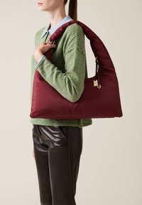 Maroon hobo bag with a textured finish and a curved, padded shape. Features a gold hardware clasp and a wide shoulder strap, set against a neutral background.