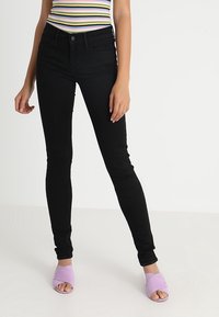 Los jeans skinny negros presentan una cintura de tiro medio y un material de denim suave y elástico. Se combinan con sandalias de plataforma de color púrpura pálido.