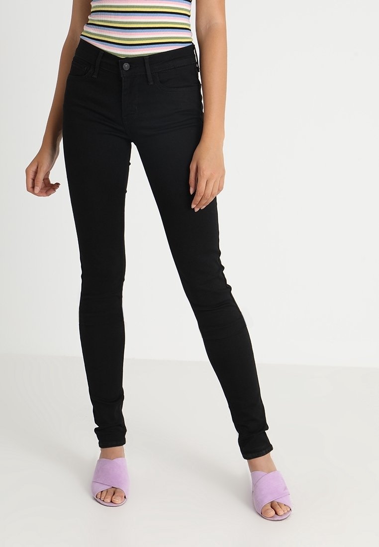 Los jeans skinny negros presentan una cintura de tiro medio y un material de denim suave y elástico. Se combinan con sandalias de plataforma de color púrpura pálido.