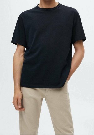 Czarna koszulka z okrągłym dekoltem, wykonana z bawełnianej mieszanki, o luźnym kroju i krótkich rękawach, zestawiona z beżowymi spodniami.