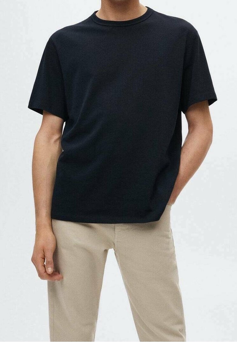 T-shirt noir à col rond en mélange de coton, doté d'une coupe décontractée et de manches courtes, associé à un pantalon beige.