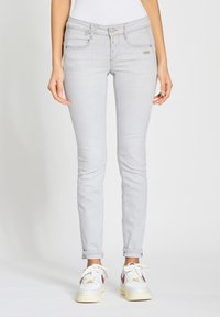 Jeans skinny gris claro con una cintura de media altura, bolsillos frontales y cierre de botón; combinados con zapatillas blancas con acentos multicolores.