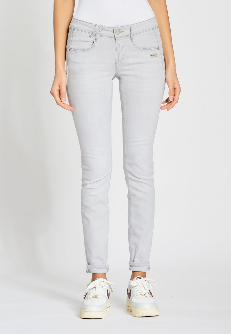 Jeans skinny gris claro con una cintura de media altura, bolsillos frontales y cierre de botón; combinados con zapatillas blancas con acentos multicolores.