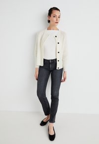 Cream-colored knit cardigan with a round neckline, button front, worn over a fitted white top and dark skinny jeans, paired with black flats.